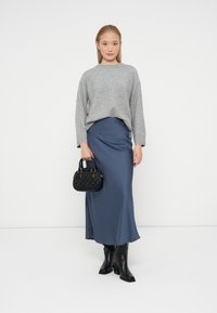 Pulover tricotat gri, fustă maxi din satin bleumarin, poșetă neagră texturată și cizme negre până la genunchi. O ținută clasică și rafinată, cu texturi netede.