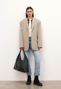 Túlméretezett bézs blézer egy fehér ing felett, alatta kockás ing, világoskék farmernadrág, fekete sarokcsizma és fekete bőr válltáska.