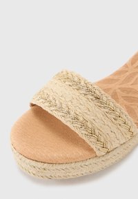 Sandale en fibre naturelle avec une large sangle tissée ornée d'accents métalliques, semelle intérieure rembourrée et semelle texturée de couleur naturelle.