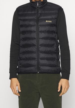 Veste matelassée noire avec logo "BOSS", portée sur une chemise noire à manches longues, associée à un pantalon vert foncé.