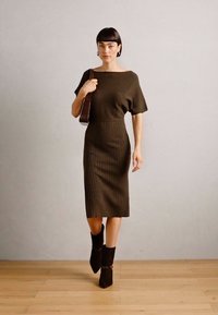 Dark olive green ribbed dress with a fitted silhouette, short sleeves, and mid-calf length. Paired with ankle boots.