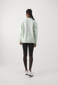 Mint green sweater, black leggings with sheer panels, and white athletic shoes. Simple design with ribbed cuffs and sporty accents.