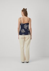 Marineblaues ärmelloses Top mit weißem Blumenmuster, kombiniert mit hellbeigen weiten Hosen. Mit dünnen verstellbaren Trägern und einem lockeren Schnitt.