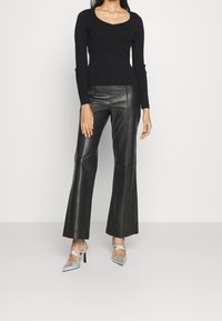 Svart ribbad tröja med rundad halsringning, kombinerad med högmidjade svarta läderbyxor med utsvängda ben och silvriga snabblinade klackar.