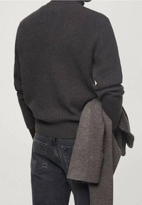 Ciemnoszary sweter o fakturze z okrągłym dekoltem, w zestawieniu z szarymi dżinsami. Jaśniejszy szary kawałek dzianiny jest zarzucony na jeden rękaw.