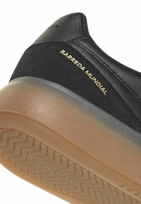 Chaussure de sport noire avec tige en suède et matière synthétique, lettrage doré "Barreda Mundial", et semelle en caoutchouc caramel avec motif en zigzag.