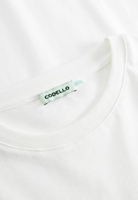 Weißes Baumwoll-T-Shirt mit Rundhalsausschnitt. Mit einem hellen Teal-Label mit der Aufschrift "CODELLO" in der Nähe des Ausschnitts. Glatte Textur.