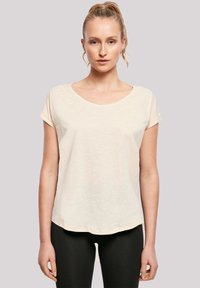 Light beige short-sleeve t-shirt with a round neckline and subtle texture, paired with black leggings, shown front-facing against a neutral background.