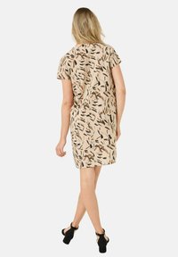 Kurzärmliges Kleid in Beige mit einem Blättermuster in Braun und Schwarz. Lockerer Schnitt, knielang und glatte Stofftextur.