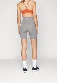 Shorts atletici grigi a vita alta e un reggiseno sportivo arancione realizzati in tessuto elasticizzato, con un logo sul retro del reggiseno e dei pantaloni.