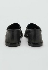 Zapatos de cuero negro con una textura suave, parte trasera redondeada y suelas de goma de perfil bajo. Presentan un diseño minimalista sin cordones.