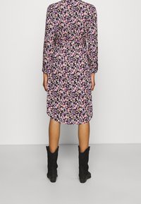 Květinové šaty s černým pozadím, zdobené růžovými a fialovými květy, s dlouhými rukávy, páskem v pase a délkou po kolena. Nosené s černými botami.