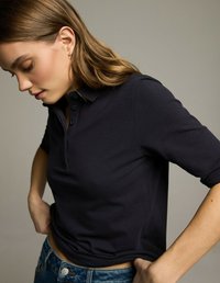 Granatowa koszulka polo z krótkim rękawem, z kołnierzykiem i zapinaniem na trzy guziki. Miękka, gładka w dotyku. Połączona z niebieskimi dżinsami.