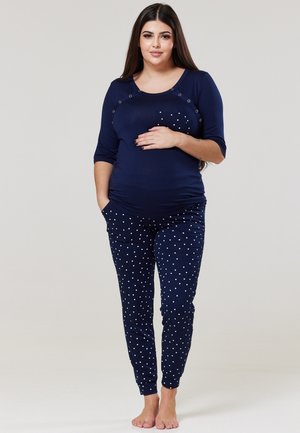 Navy blue maternity top with short sleeves and snap detail; paired with navy polka dot pants featuring pockets and tapered cuffs.