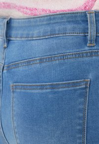 Τζιν παντελόνι, ανοιχτό γαλάζιο με λεία υφή. Διαθέτει πίσω τσέπη και αντίθετη ραφή κατά μήκος της μέσης και στη ραφή της τσέπης.