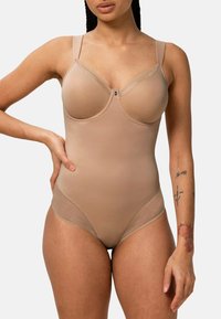 El body nude presenta copas acolchadas, acentos de malla transparente, tirantes ajustables y una textura de tela suave y elástica. Detalles en hardware plateado.