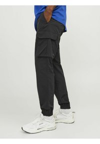 Sorte cargo-bukser med elastiske manchetter, der har sidelommer og en løs pasform, parret med hvide sneakers og en blå top.
