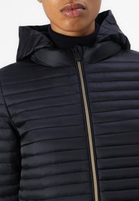 Veste noire matelassée avec capuche, dotée d'une fermeture éclair dorée et d'une texture lisse. Le design inclut des coutures horizontales pour un aspect structuré.