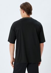 Sort kortærmet polo skjorte med en glat tekstur og en krave med diskrete beige accenter. Enkel, afslappet pasform med et sømløst design.