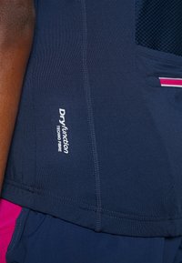 Primer plano de tela deportiva azul marino con el texto "Dry Function Techno Fibre" y un pequeño bolsillo con cremallera con detalles en rosa y blanco.