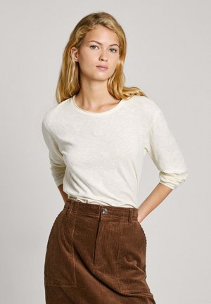 Light cream long-sleeve top in soft fabric features a round neck. Paired with a brown corduroy skirt, showing textured fabric and front button.