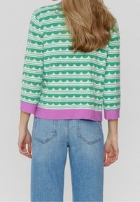 Pull côtelé rayé vert et blanc avec motifs ondulés, ourlet violet et manches trois-quarts, associé à un jean bleu clair.