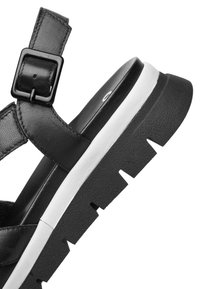 Sandalia negra con tiras de cuero texturizado, hebilla ajustable y una suela gruesa blanca y negra con un dibujo de tracción tipo taco.