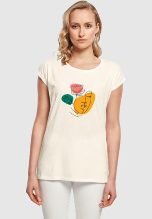 T-shirt couleur crème à manches courtes retroussées, présentant un motif floral abstrait en rose, vert et orange sur le devant.