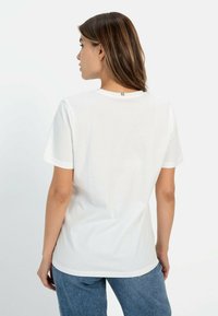 Hvid bomulds t-shirt med korte ærmer, rund hals og en syet detalje bagpå. Stof virker glat og let.
