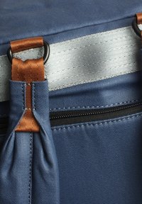 Blaue Tasche aus strukturiertem Material mit silbernen Akzenten, kupferfarbenen Trägern, einer Reißverschlusstasche und kreisförmigen Beschlägen.