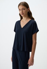 Top blu navy con scollo a V e maniche corte, realizzato in tessuto liscio. Vestibilità ampia e orlo che cade appena sopra la vita. Adatto per abbigliamento informale.