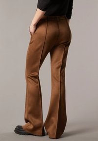 Pantaloni marroni a palazzo realizzati in tessuto liscio, caratterizzati da una vita aderente, tasche frontali e un design sartoriale con una leggera lucentezza.