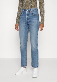 Högmidjade blå denimjeans med rak skärning, ljus tvätt och synliga sömmar, ihop med en långärmad topp i leopardmönster och vita sneakers.