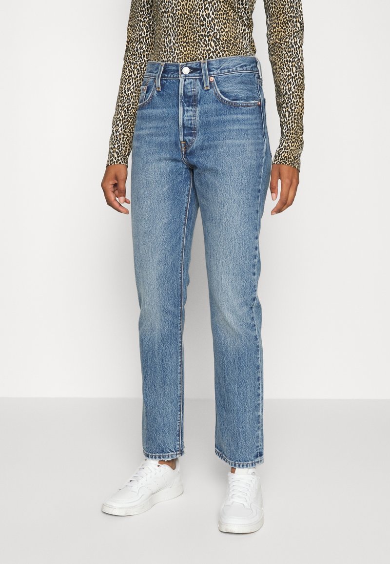 Högmidjade blå denimjeans med rak skärning, ljus tvätt och synliga sömmar, ihop med en långärmad topp i leopardmönster och vita sneakers.