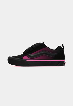 Low-top sneaker with black and dark pink panels, black laces, wave detail, and pink stripe on black rubber sole.