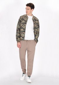 Camo bomberjack in groen en beige, wit T-shirt, beige joggers en witte sneakers. Casual fit met ribgebreide boorden en zoom.