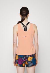 Top a canotta color pesca con spalline incrociate nere, con un piccolo logo Nike sul retro. Abbinato a pantaloni corti scuri con fantasia floreale.