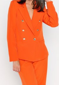 Orange double-breasted blazer with metallic buttons, notch lapels, and side pockets. Smooth, lightweight fabric with a tailored fit.