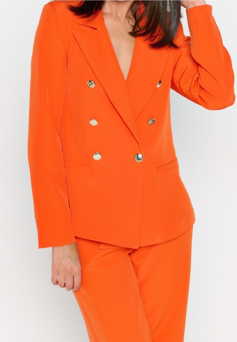 Orange double-breasted blazer with metallic buttons, notch lapels, and side pockets. Smooth, lightweight fabric with a tailored fit.