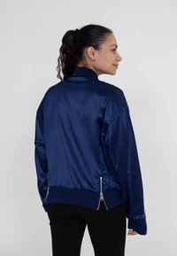 Marineblaue Satin-Bomberjacke mit hohem Kragen, gerippten Bündchen und doppelten Reißverschlusstaschen am Saum, mit einer glatten Textur und lockerer Passform.