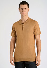 Polo a maniche corte in materiale a maglia color marrone chiaro, con colletto, patta con tre bottoni e orlo a costine. Dettaglio logo discreto sul petto.