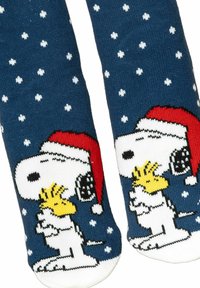 Calze lavorate a maglia in blu con motivo a fiocco di neve bianco. Presentano Snoopy e Woodstock con cappelli festivi. Il materiale sembra morbido con una finitura testurizzata.