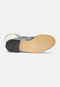 Zapato de cuero negro con una textura suave, que presenta una suela beige y un acento negro en el talón. Muestra un diseño y acabado minimalistas.
