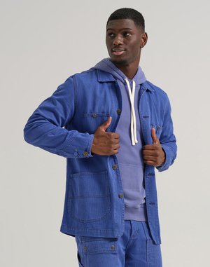 Blue corduroy jacket with a textured finish, featuring chest and side pockets, paired with a light blue hoodie and matching trousers.