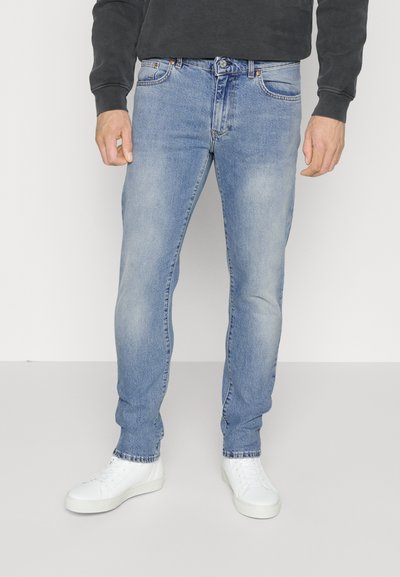 Jeans in denim blu chiaro con vestibilità slim, caratterizzati dal classico design a cinque tasche, lavaggio sbiadito e vita media, abbinati a sneakers bianche.