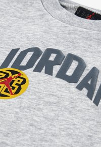 Γκρι φούτερ με έντονο σκούρο γκρι κείμενο "JORDAN" και κυκλικό λογότυπο με κίτρινο φόντο και κόκκινο γραφικό. Απαλή υφή, στρογγυλή λαιμόκοψη.