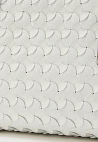 Λευκή δερμάτινη τσάντα με υφή, χαρακτηριζόμενη από κυκλικά επικαλυπτόμενα λέπια με ραμ μένες λεπτομέρειες, δημιουργώντας ένα μοτίβο από εναλλασσόμενους ημικύκλους.