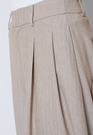 Bēša krāsas augsta vidukļa bikses ar priekšējām kroku krokām, jostas cilpām un smalku zivju kaulu rakstu, valkātas ar baltu augšu.