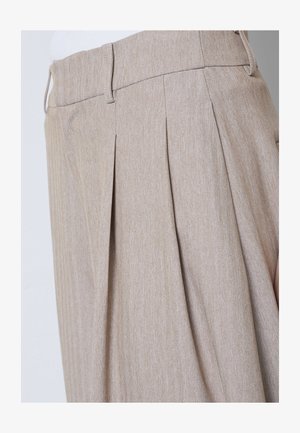Béžové nohavice s vysokým pásom so záhybmi vpredu, pútkami na opasok a jemným vzorom rybej kosti, nosené s bielym topom.