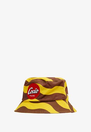 Bucket hat i brun och gul vågmönster, med en röd cirkulär patch som har ordet "Cocio" och "Sedan 1951" tryckt på.